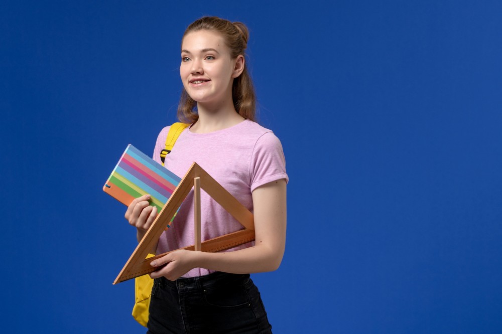 front-view-young-female-pink-t-shirt-holding-wooden-triangle-figure-copybook-blue-wall.jpg